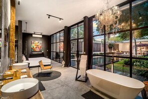 A modern bathroom with a freestanding bathtub, a large window, and a painting on the wall. - Loft Volcano by Alfred in Bali - Stylish 2 BR Loft w Pool Garden Ricefields View (Ubud)