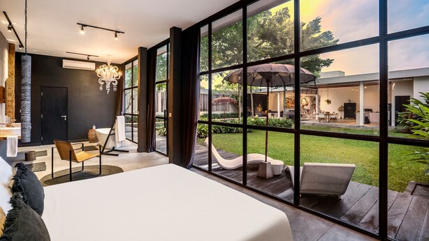 A modern bedroom with a large window, a chandelier, and a view of the outdoor patio. - Loft Volcano by Alfred in Bali - Stylish 2 BR Loft w Pool Garden Ricefields View (Ubud)