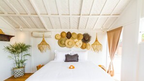 A neatly made bed with a white bedspread, a decorative wall hanging of woven hats, a potted plant, and a hanging light fixture. - Villa M by Alfred in Bali - Stunning Family Villa With Pool at Seminyak Beach (Seminyak)