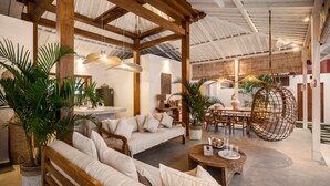Un vaste espace de vie doté d’un plafond en bois, d’un ensemble de canapés, de luminaires suspendus et d’une table à manger avec des chaises.