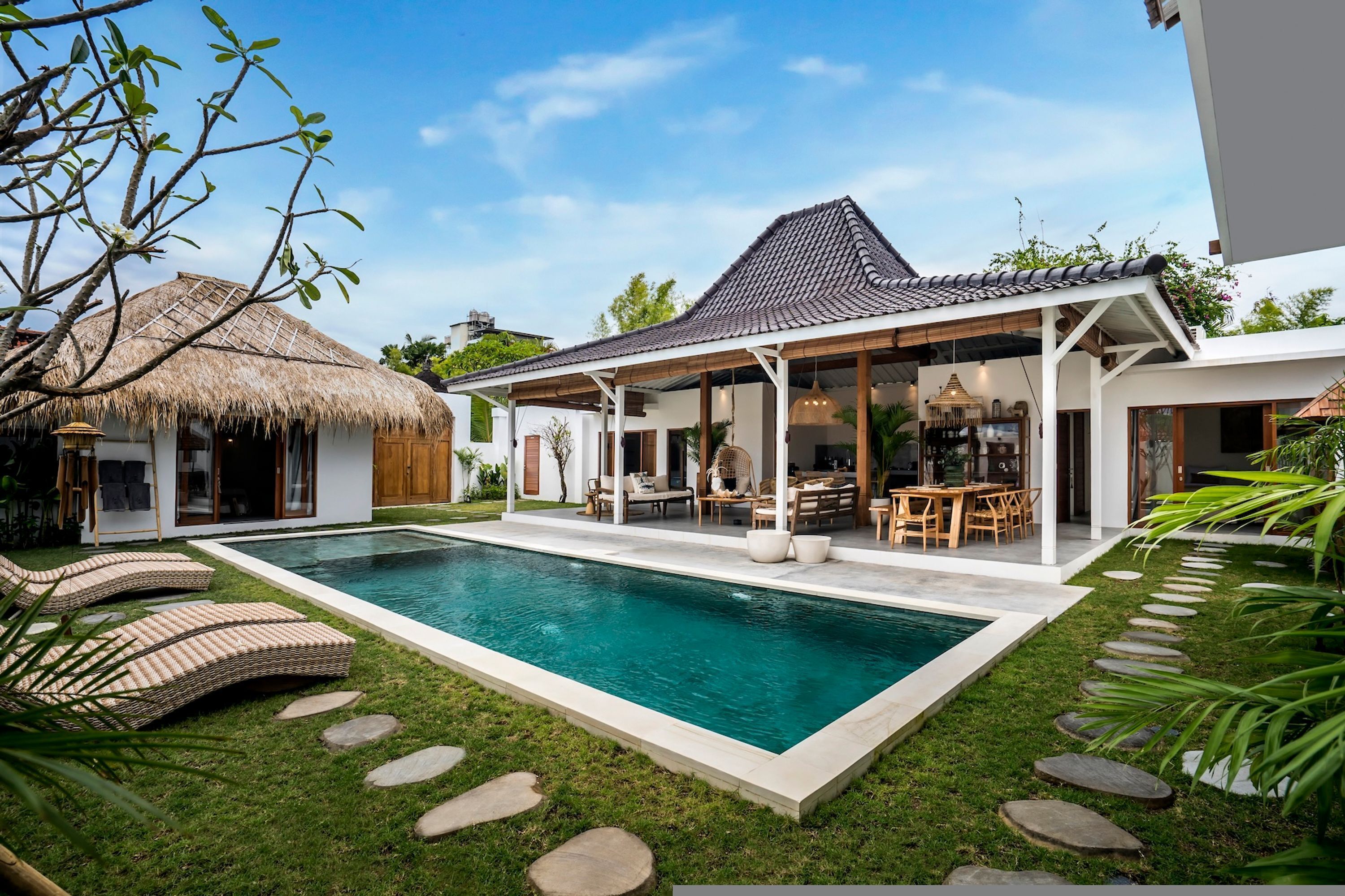 A modern house with a swimming pool, a thatched-roof structure, and a covered outdoor seating area.