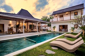Ein zweistöckiges Haus mit Swimmingpool, Gartenmöbeln und einem gepflegten Rasen.