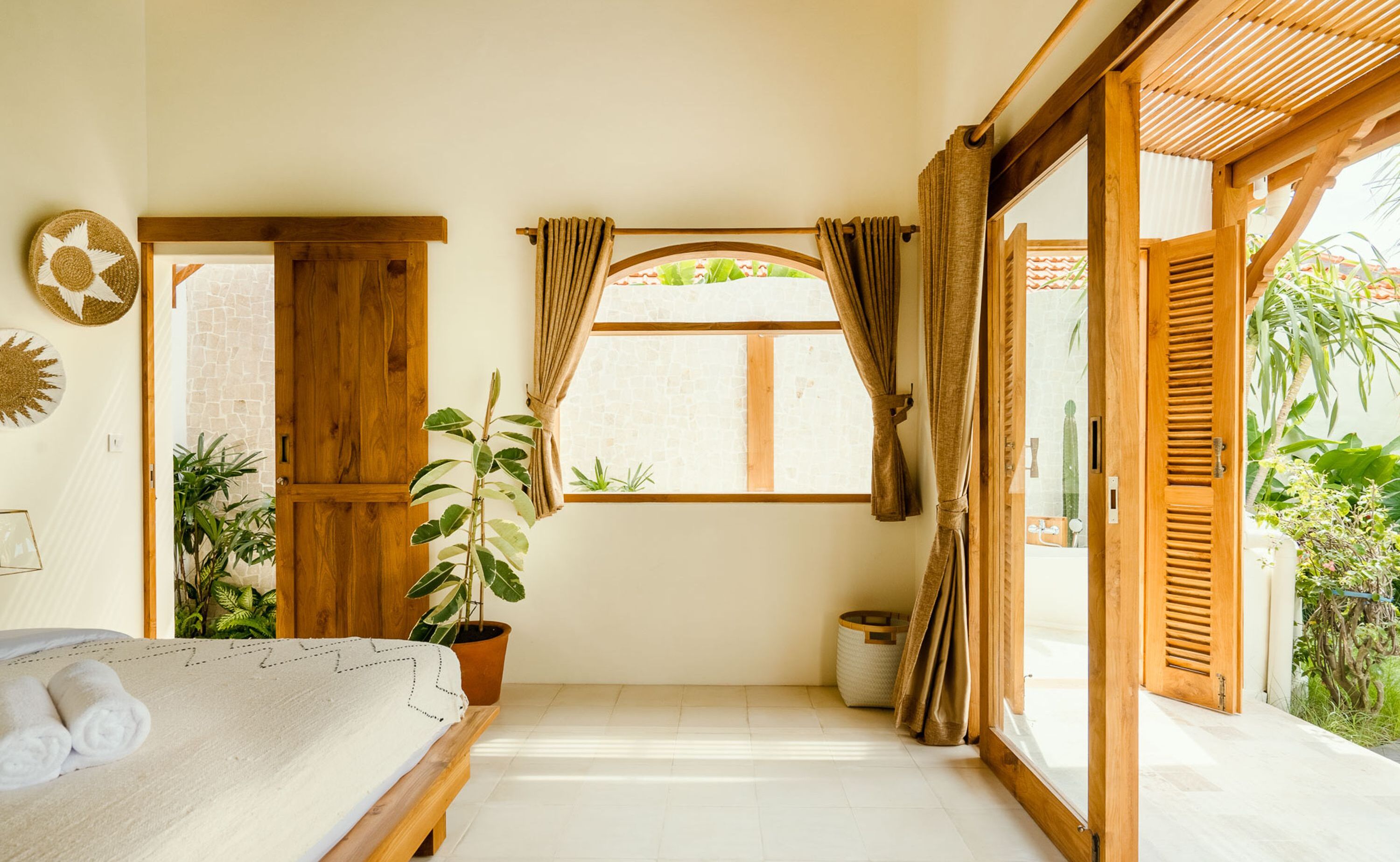 Un dormitorio con cama, ventana con cortinas, planta en maceta y vista al exterior.