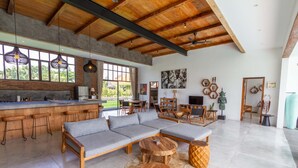 A spacious living area with a large sofa, wooden coffee table, and a kitchen area with bar stools. - Villa Maje by Alfred in Bali - Tropical 3BD Villa w Pool Near Batu Belig Beach (Seminyak)