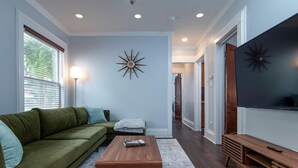 A living room with a green sofa, a wooden coffee table, a flat-screen TV, and a decorative wall piece. - Fully Stocked Kitchen,  AC,  Wi-Fi, W/D,  Near Baseball and Walk to Downtown (Oneonta)