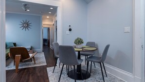 A dining area with a round table, grey chairs, and a potted plant. - Fully Stocked Kitchen,  AC,  Wi-Fi, W/D,  Near Baseball and Walk to Downtown (Oneonta)
