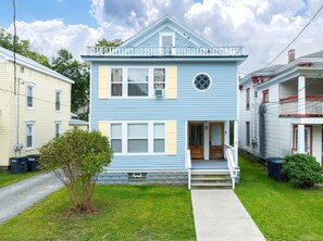 A two-story house with a front porch, a small front yard, and a stone foundation. - Fully Stocked Kitchen,  AC,  Wi-Fi, W/D,  Near Baseball and Walk to Downtown (Oneonta)
