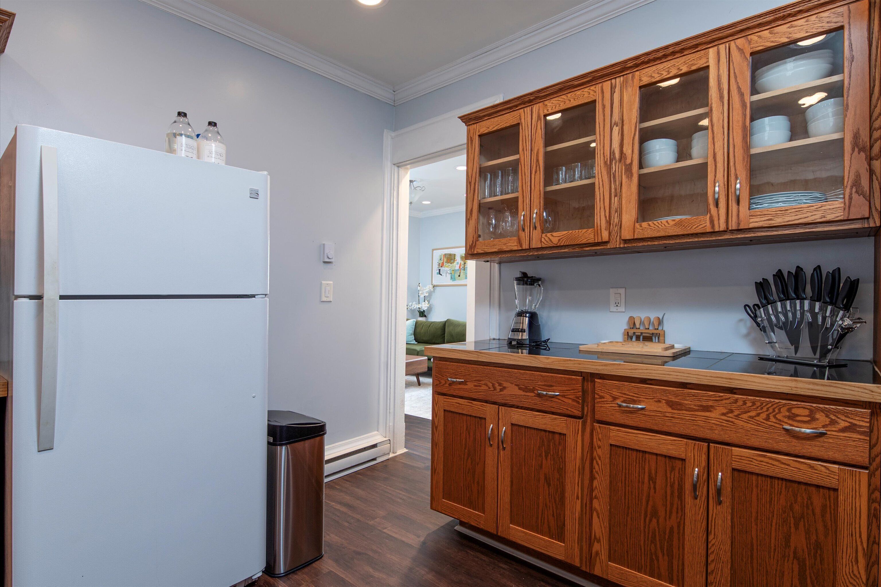 A kitchen with wooden cabinets, a white refrigerator, and a trash bin.