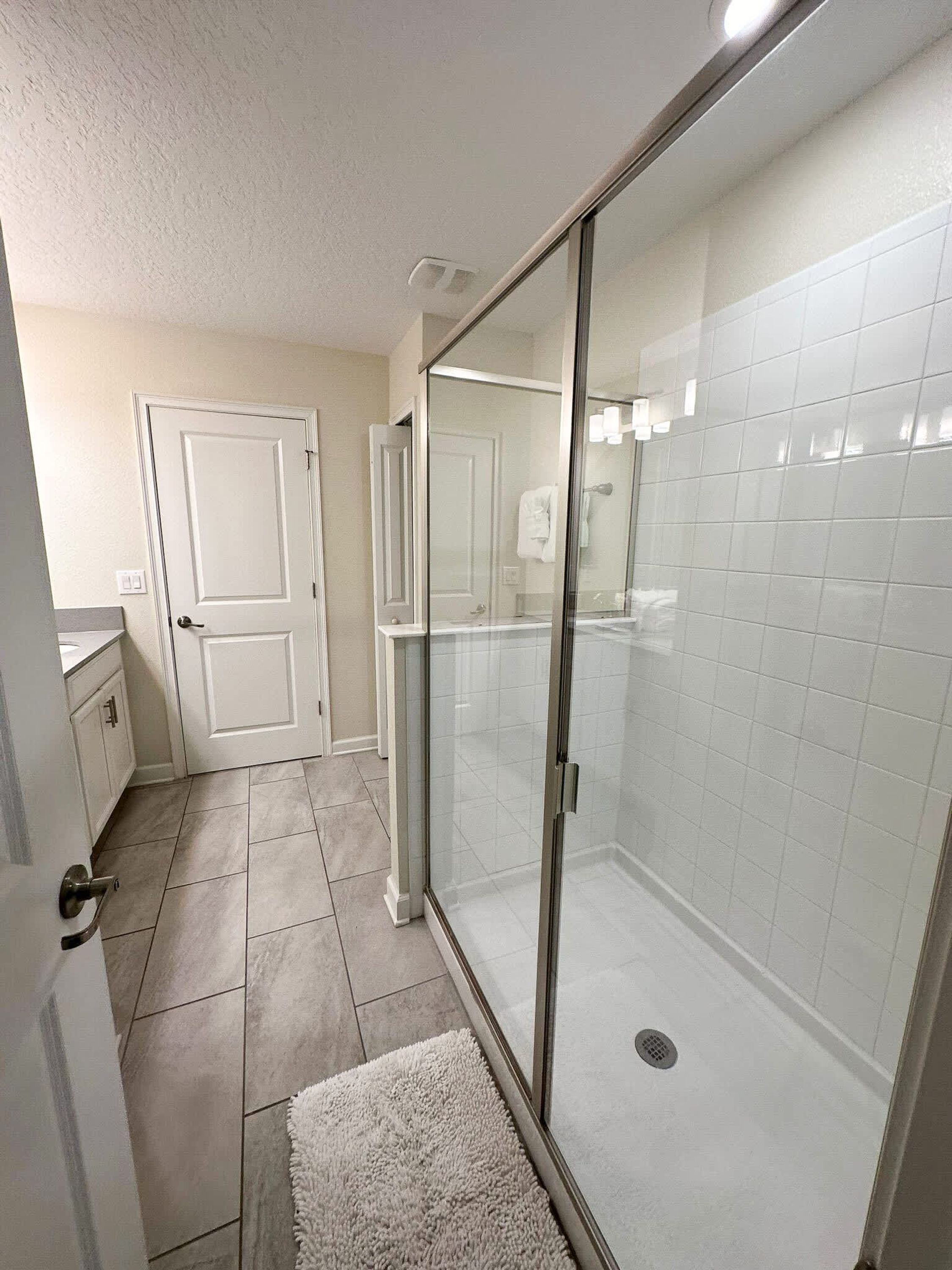 A modern bathroom with a glass shower enclosure, white tiled walls, and a visible toilet.