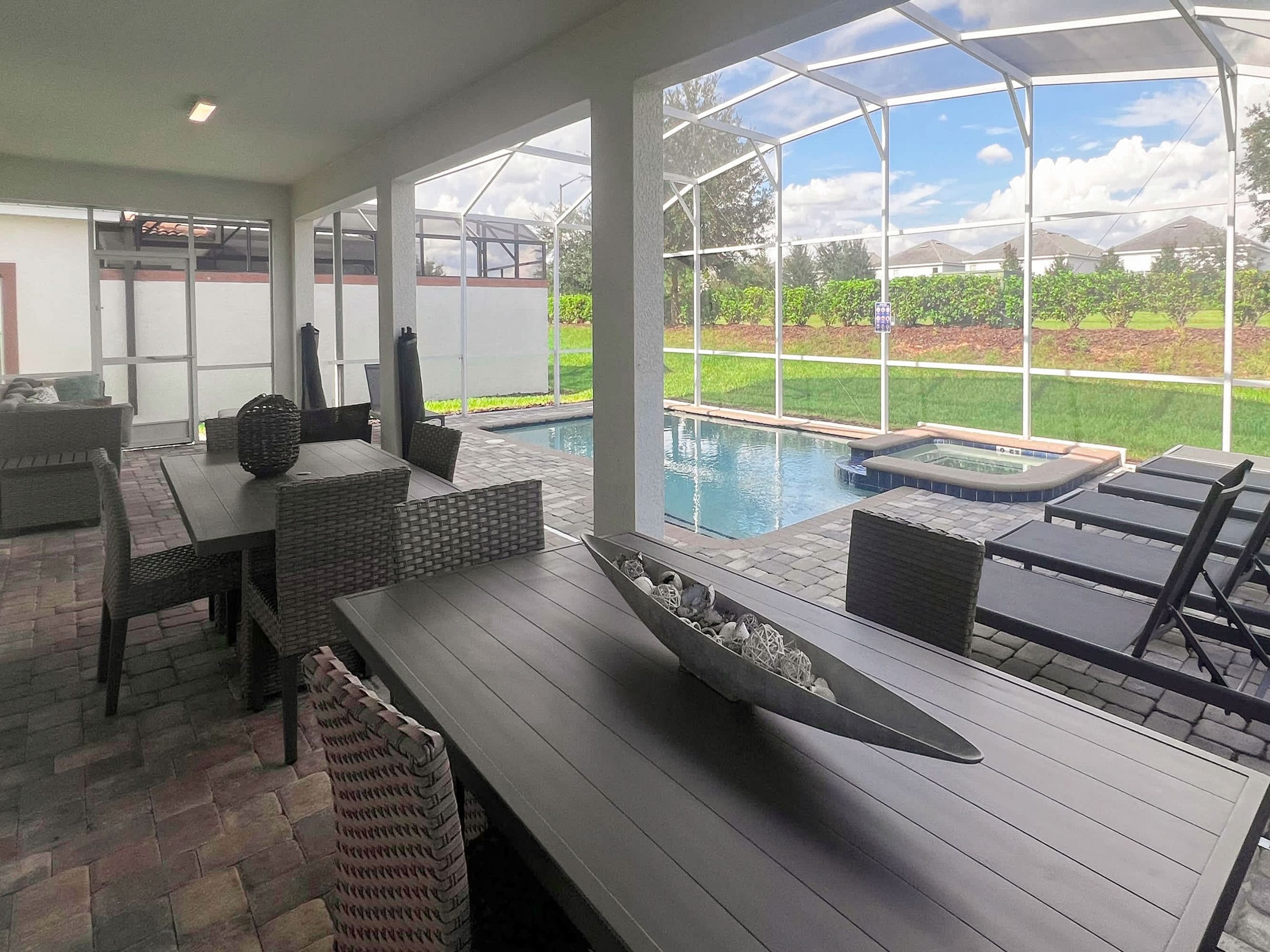 Un patio couvert avec une piscine, du mobilier d’extérieur et une vue sur un jardin aménagé.