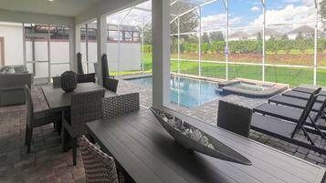 Un patio couvert avec une piscine, du mobilier d’extérieur et une vue sur un jardin aménagé.