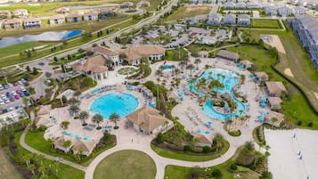 An aerial view of a resort with multiple swimming pools, a central gazebo, and a beach area.