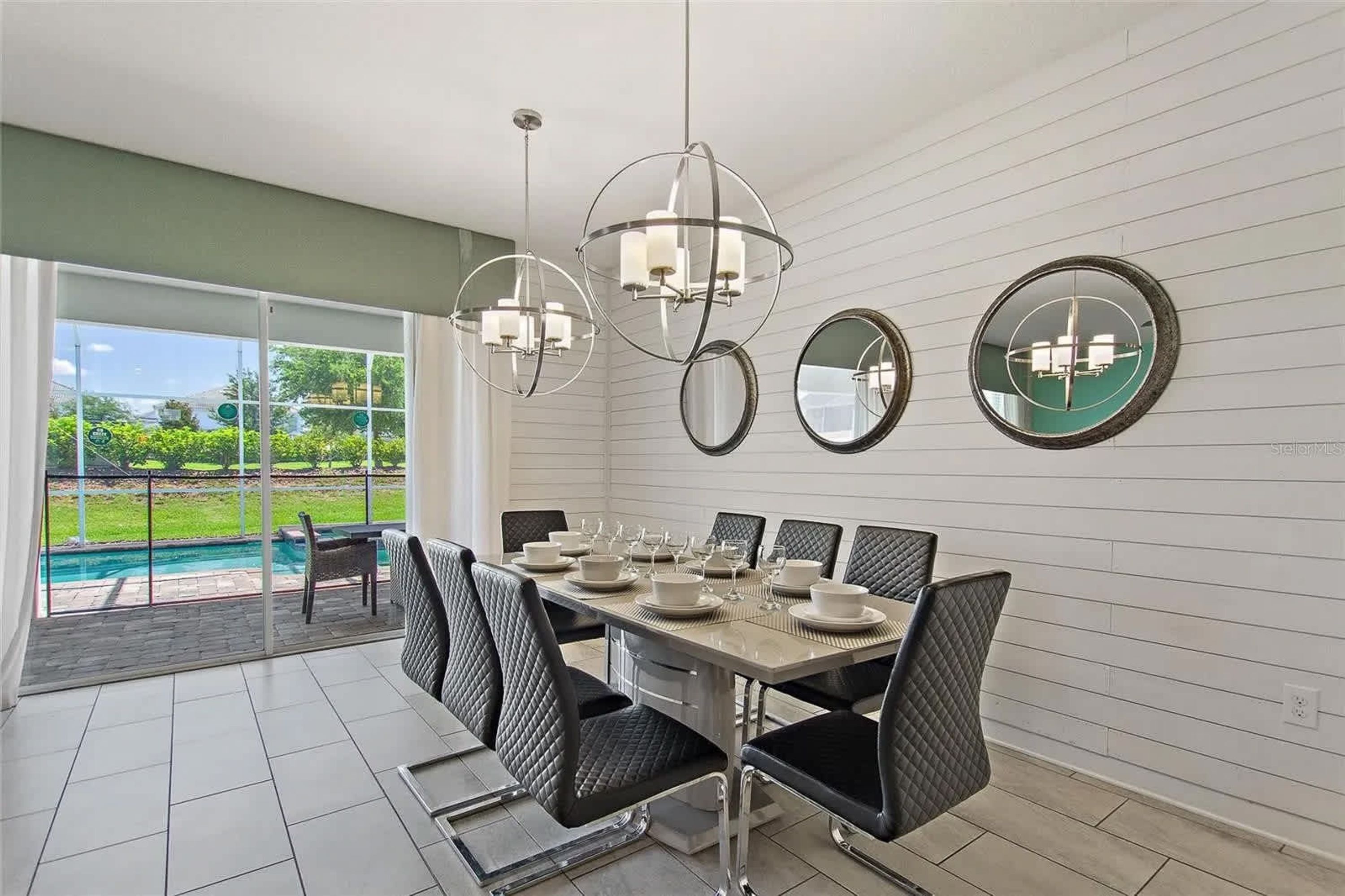 Un espace repas avec une grande table dressée pour six personnes, entourée de chaises noires, et une piscine visible à travers des portes vitrées.