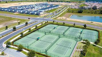 A large tennis court complex with multiple courts, surrounded by a road and residential buildings.