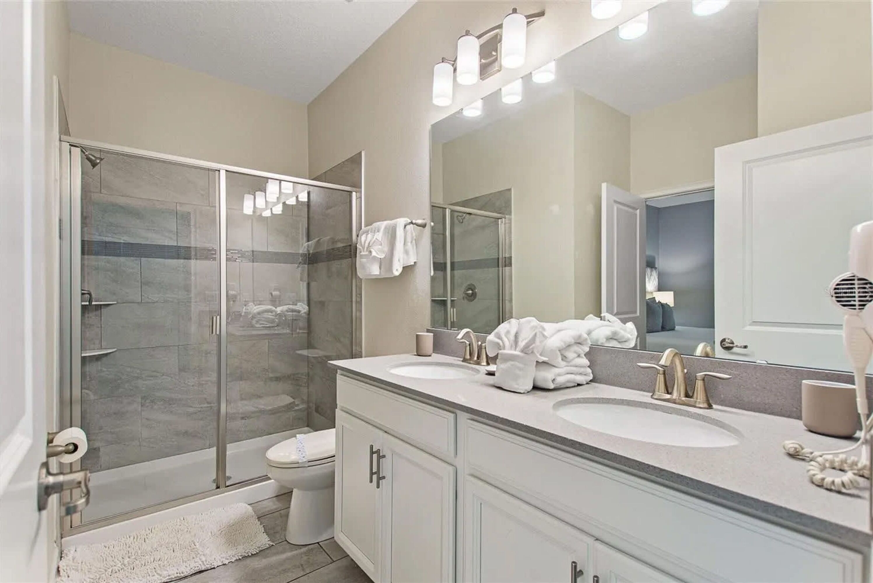 A modern bathroom with a glass-enclosed shower, two sinks, and a large mirror.