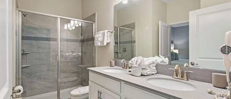 A modern bathroom with a glass-enclosed shower, two sinks, and a large mirror.