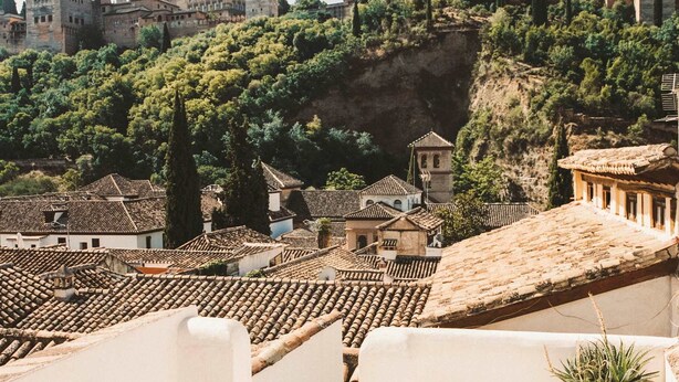 Una terraza con paredes blancas y una planta en maceta, con vistas a un pueblo histórico con tejados de terracota y un castillo destacado en una colina.
