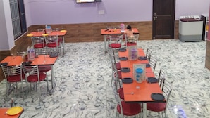 Zona pranzo con diversi tavoli e sedie, una televisione montata a parete e una porta sullo sfondo.