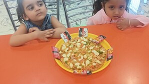 Due bambini seduti a un tavolo con una pizza e salse.