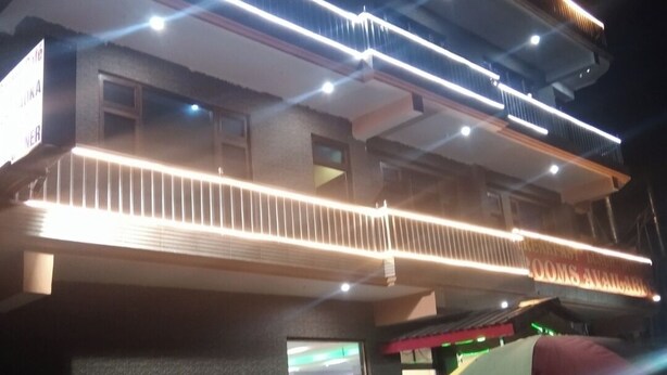 Un edificio con diversi piani, illuminato da luci LED lineari. Sono presenti aree salotto all'aperto con sedie e tavoli rossi.