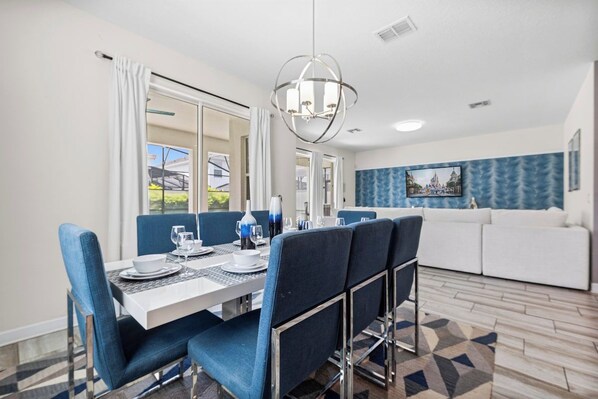 A dining area with a table set for four, blue upholstered chairs, and a modern chandelier.