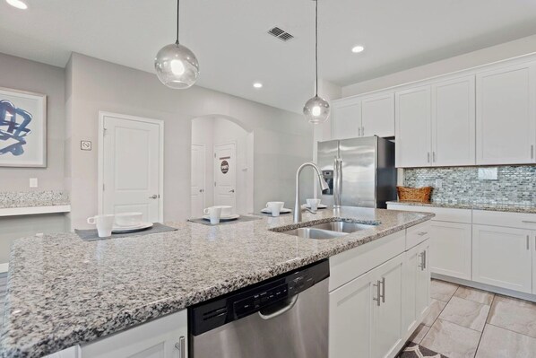 A modern kitchen with granite countertops, stainless steel appliances, and white cabinetry.
