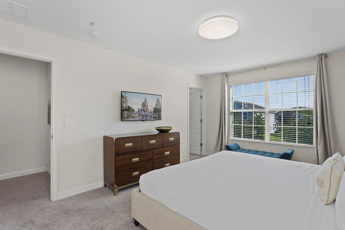- Unwind in this bright bedroom with a large window offering scenic views - Elegant dresser and wall-mounted TV for convenience and entertainment - Comfortable and serene ambiance, perfect for relaxation after a long day