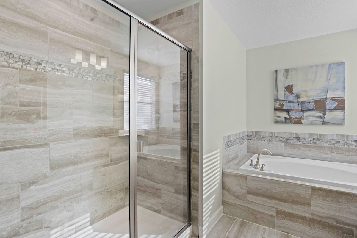 - A bathroom featuring a glass walk-in shower with modern tile design - Large bath tub for ultimate relaxation, accented with elegant stonework - Bright and serene, perfect for unwinding in a spa-like atmosphere