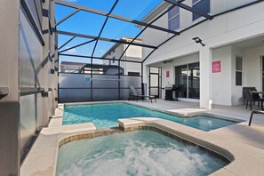 A pool area with a glass-enclosed structure, a hot tub, and a seating area with chairs and a table.