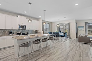 A modern kitchen with a central island, bar stools, and a dining area with a view. - Kissimmee Bliss: 6BR Pool Home w Game Room (Kissimmee)
