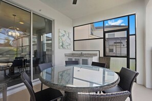 A modern dining area with a glass-top table and wicker chairs, a kitchen with a sink and cabinets, and a large sliding glass door leading to an outdoor space.