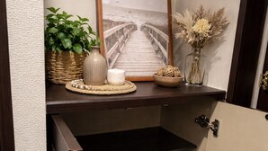 A hallway with a wooden shelf displaying a framed picture, a potted plant, a candle, and decorative items.