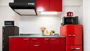 A kitchen with red cabinets, a black microwave, a red refrigerator, and a stainless steel sink.