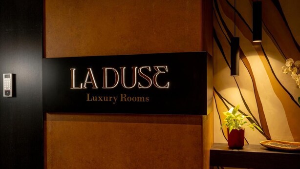 Segnaletica per 'LA DUSÉ Luxury Rooms' dal design moderno, con una pianta in vaso e una parete decorativa.