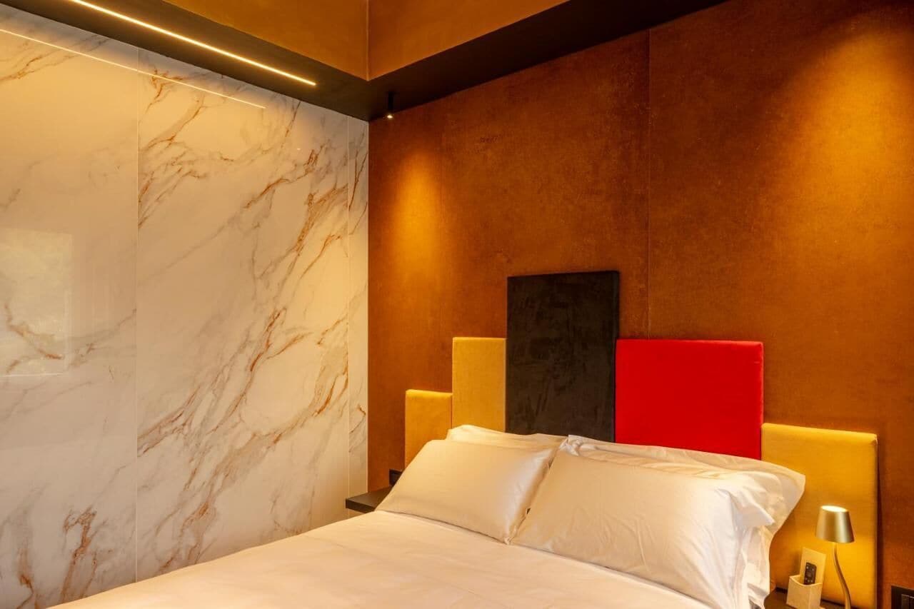 Camera d'albergo con parete in marmo, letto con lenzuola bianche, parete di accento rossa e una moderna testiera.