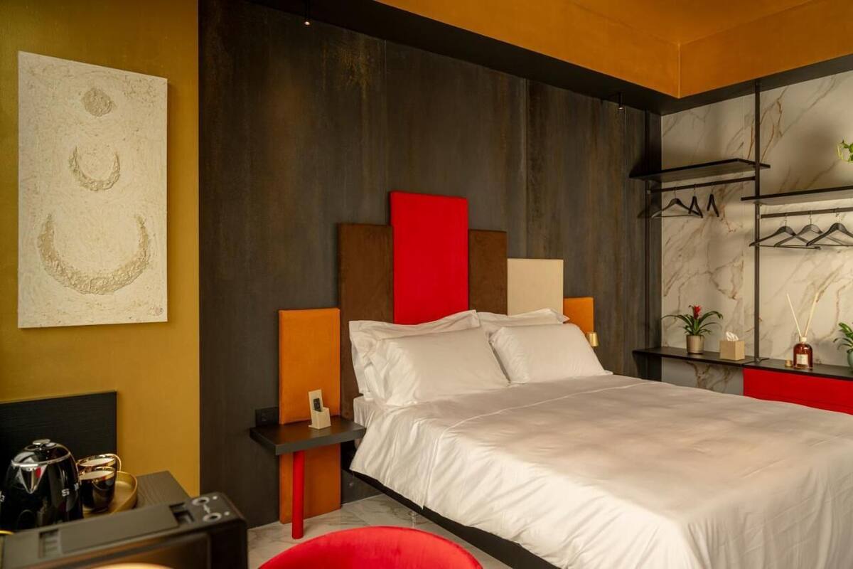 Habitación de hotel moderna con una cama grande, una mesita de noche, una silla roja y un estante con plantas fijado a la pared.