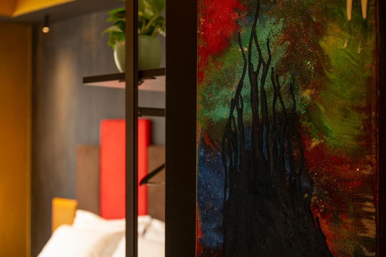 A room with a bed, a red chair, and a painting on the wall.