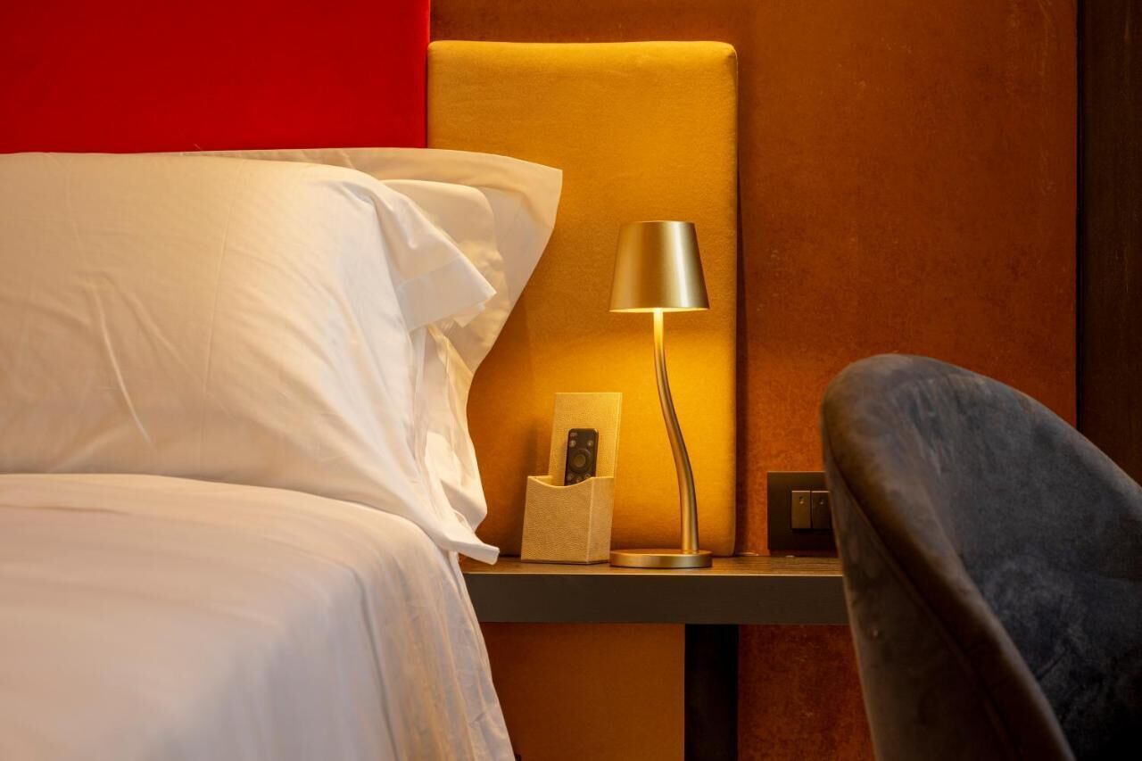 A neatly made bed with white linens, a bedside table with a lamp, a remote control, and a chair.