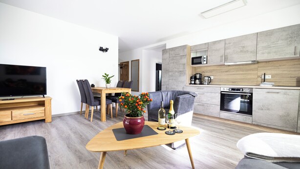 A modern living room with a flat-screen TV, a wooden coffee table with a vase of flowers, and a grey sofa. - Vacation residence Hunsrück Hochwald (Mörschied)