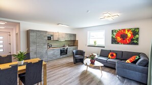 A modern living room with a grey sofa, a wooden dining table, and a kitchen in the background. - Vacation residence Hunsrück Hochwald (Mörschied)