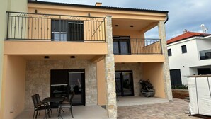 Una casa de dos pisos con balcón, pilares de piedra y un patio cubierto con mesa y sillas.