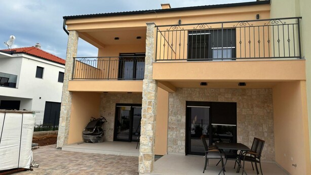 Un edificio de dos pisos con balcón, pilares de piedra y un patio con mesa y sillas.