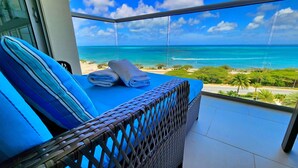 Een balkon met een bed, uitzicht op de oceaan en een tropisch landschap.