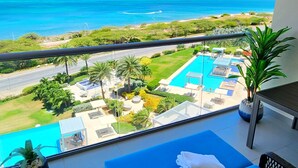 Een balkon met uitzicht op de oceaan, een zwembad en een loungehoek met een blauwe bank en kussens.