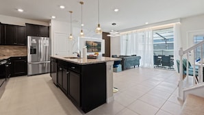A modern kitchen with dark cabinetry, stainless steel appliances, and a large island.