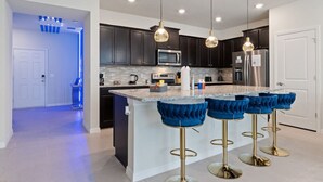 A modern kitchen with dark cabinets, stainless steel appliances, a marble island, and blue bar stools.