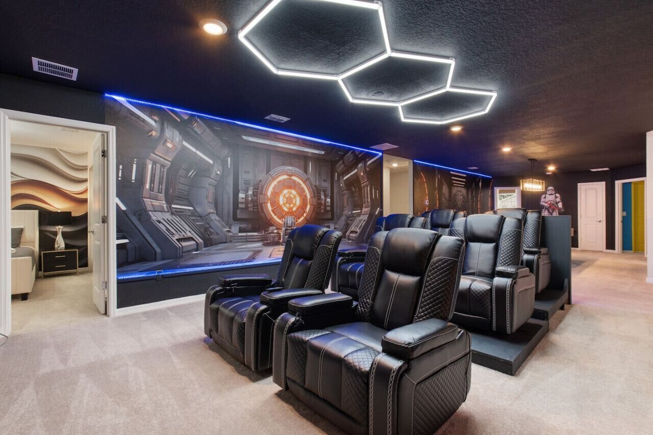 A room with a futuristic design, featuring a large mural of a space station, black leather chairs, and a hexagonal light fixture on the ceiling.
