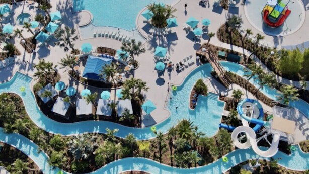 Vue aérienne d’un complexe hôtelier doté d’une grande piscine centrale, de plusieurs toboggans aquatiques et de palmiers.