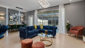 Un salon moderne avec un canapé bleu, une table basse en verre et un coin repas avec des chaises vertes.
