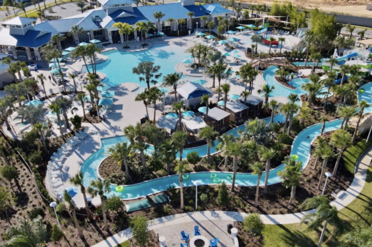 Luchtbeeld van een resort met verschillende zwembaden, palmbomen en terrasjes.